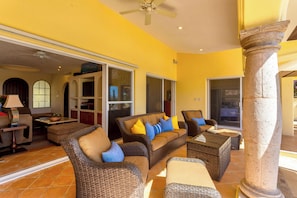 A spacious living area with wicker furniture, a ceiling fan, and a view through a glass door.