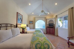 A hotel room with two beds, a ceiling fan, a TV, and a window with curtains.