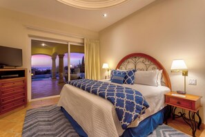 A bedroom with a bed, a TV, a nightstand, and a view of the outside. - Villa Agave Azul | 5BR Ocean View Villa | Pool, Jacuzzi & Golf Views (Cabo del Sol)