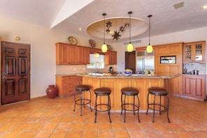 A kitchen with wooden cabinets, a central island with stools, a refrigerator, and pendant lighting.