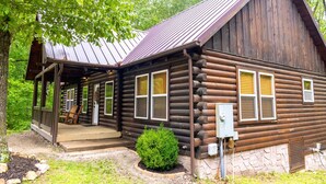 Eine Blockhütte mit Veranda, kleinem Garten und einer Metallbedachung.