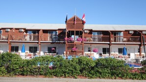A multi-story hotel with balconies, outdoor seating, and flags. - Sea Drift Motel (Old Orchard Beach)
