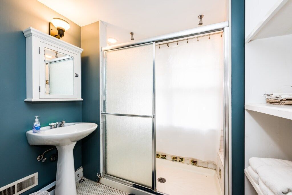 A bathroom with a white pedestal sink, a glass shower enclosure, and a white vanity with a mirror.
