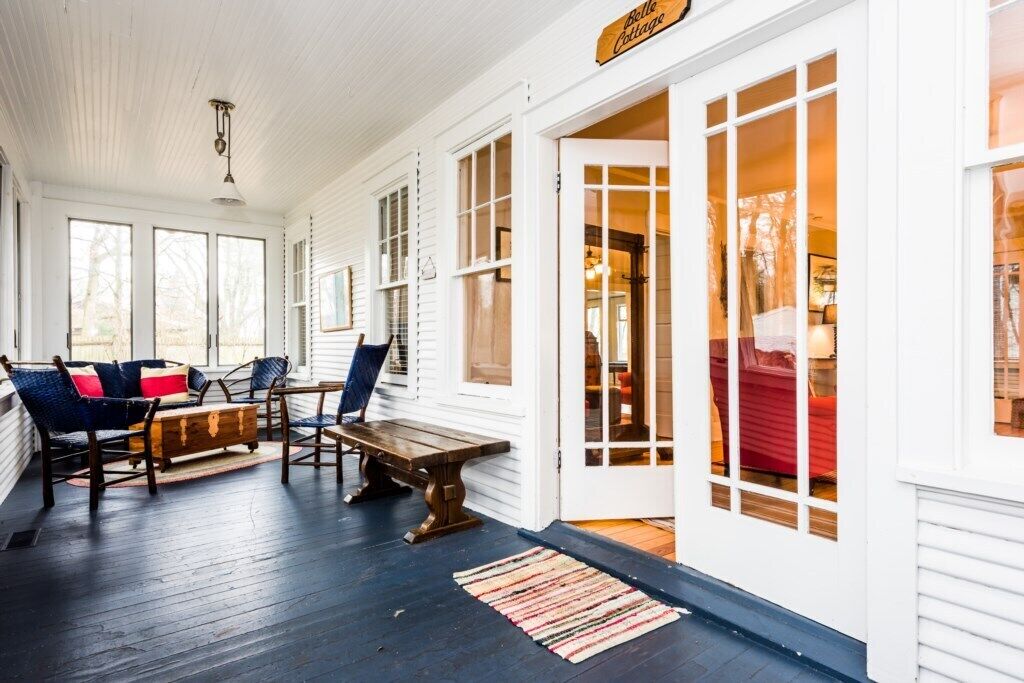 A cozy porch with a bench and chairs, a wooden table, and a rug.