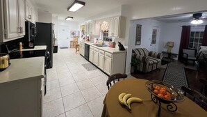Una cocina amplia con armarios blancos, un comedor con una mesa para dos, y una sala de estar con sofá y sillones.