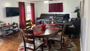 Un comedor con una mesa redonda, sillas y un televisor al fondo.