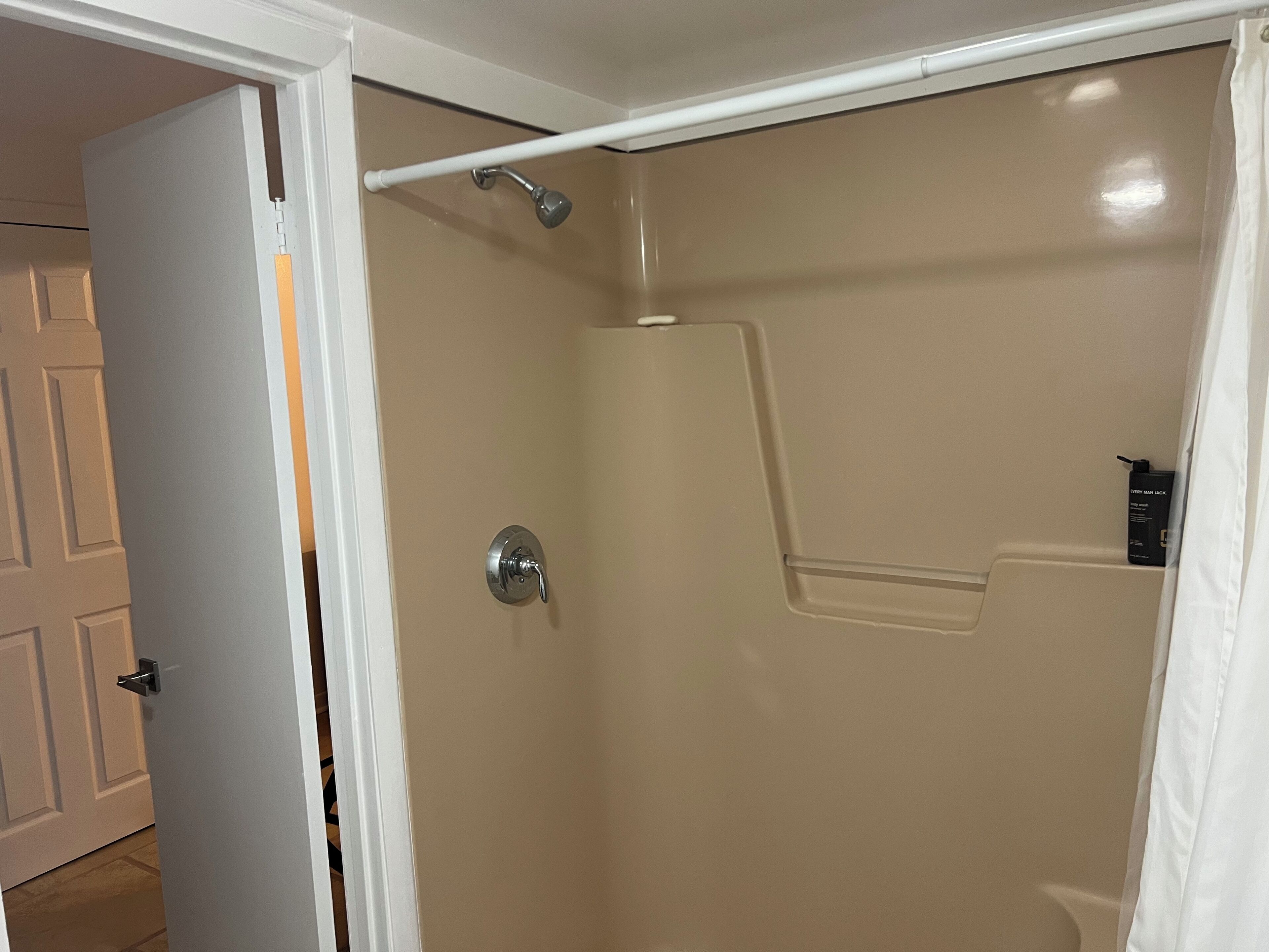 Un baño con pared color beige, ducha con cortina blanca y puerta con picaporte plateado.