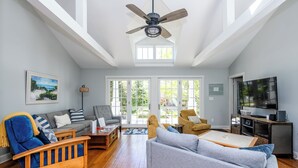 A spacious living room with a ceiling fan, a television, and a large window.