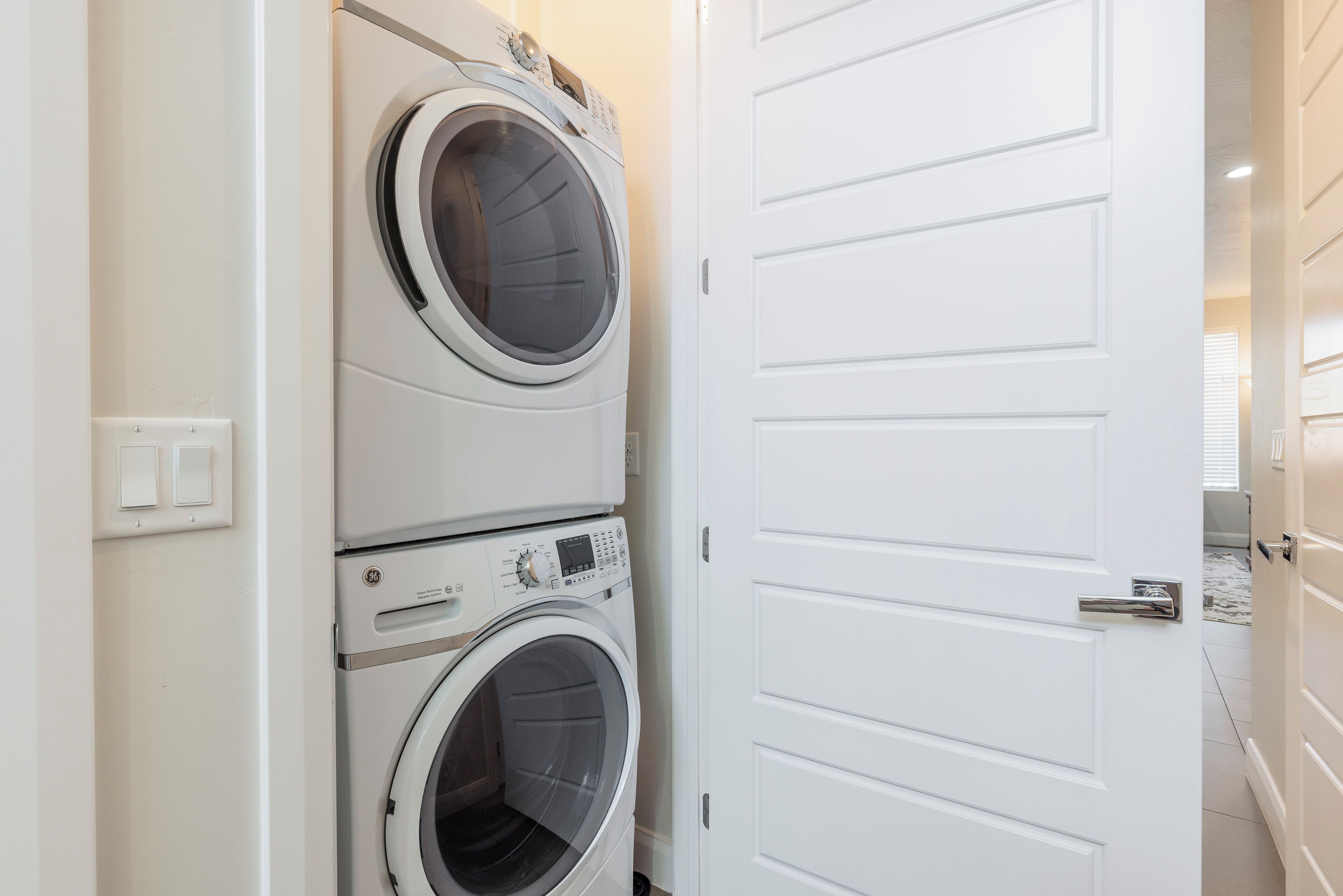 Un cuarto de lavandería con dos lavadoras de carga frontal apiladas y una puerta blanca.