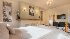 Une chambre à coucher avec un grand lit, une cheminée, un téléviseur et des œuvres d’art accrochées aux murs.