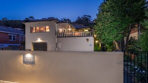 Une maison moderne à deux étages, dotée d’un balcon, d’un garage et d’un éclairage extérieur soigné.