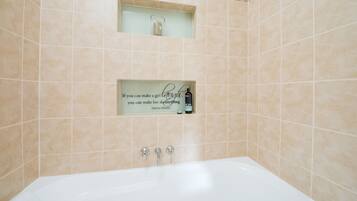 A bathroom with beige tiles, a white bathtub, and a quote sign on the wall.