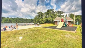 A playground with a slide and climbing structures, a small building, and a grassy area with a lake in the background. - Beautiful Two Story Home In long pond  pa (Long pond)