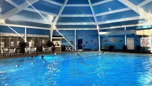 An indoor swimming pool with a high ceiling and a poolside area with chairs and a table. - Beautiful Two Story Home In long pond  pa (Long pond)