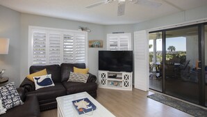 A living room with a brown leather sofa, a flat-screen TV on a white stand, and a sliding glass door leading to an outdoor patio. - CRC 1105 - Ground Floor Condo with Great Pool & Beach Access (St Augustine)