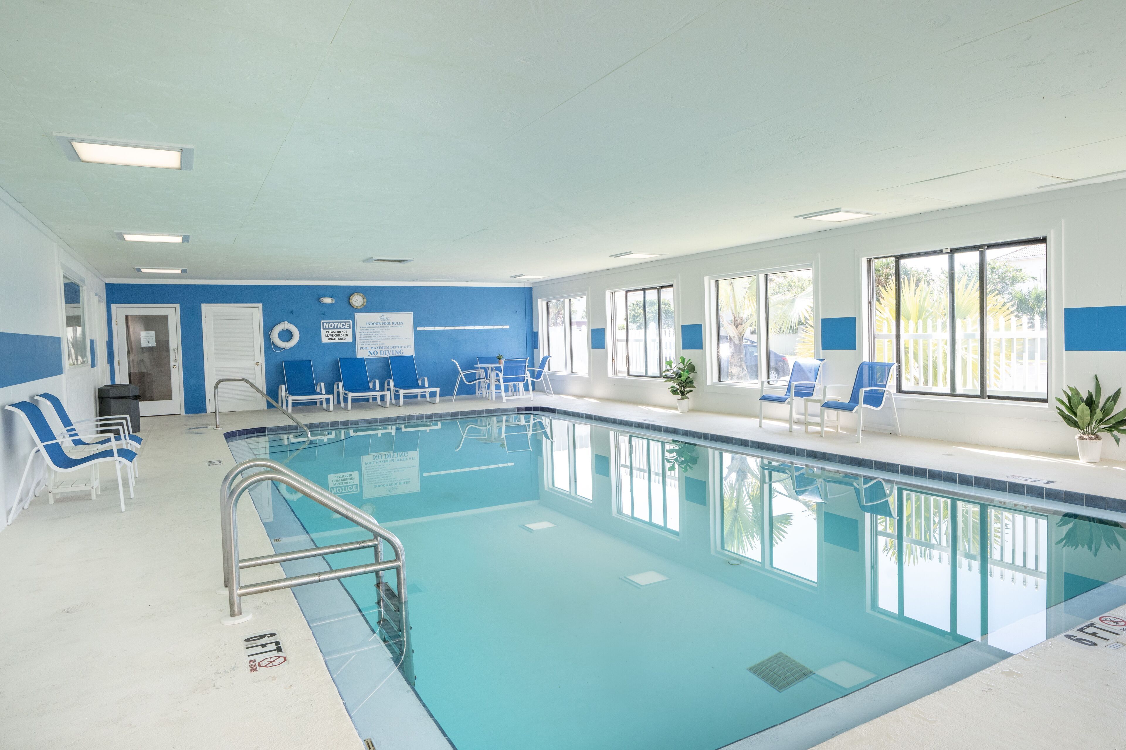 Une piscine intérieure à l’eau d’un bleu limpide, entourée de murs bleus et blancs, et dotée de plusieurs chaises longues et d’un panneau de signalisation de sécurité.