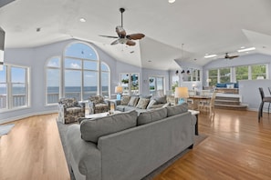 A spacious living room with a large gray sectional sofa, a patterned armchair, and a dining area with a table and chairs. - La Dolce Vita: Soundfront, Shared Pool, Hot Tub (Corolla)