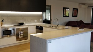 A modern kitchen with built-in appliances, a central island, and a dining area with a dark-colored sofa.