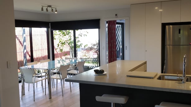A modern kitchen with a central island, bar stools, and a dining area with chairs and a table.