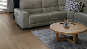 A modern living room with a beige sectional sofa, a round wooden coffee table, and a patterned rug.