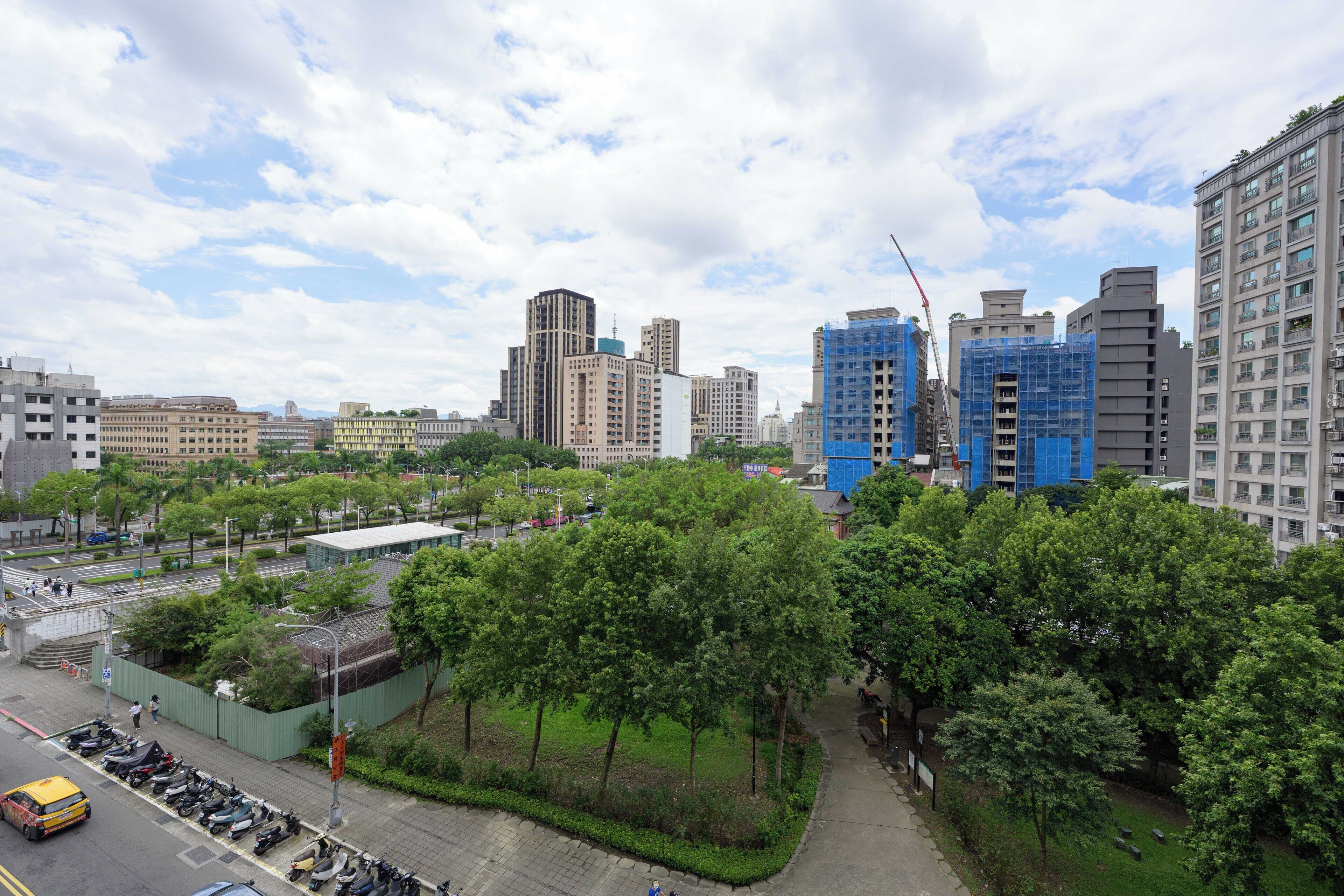 A cityscape with modern buildings, a parking area, and a green park.
