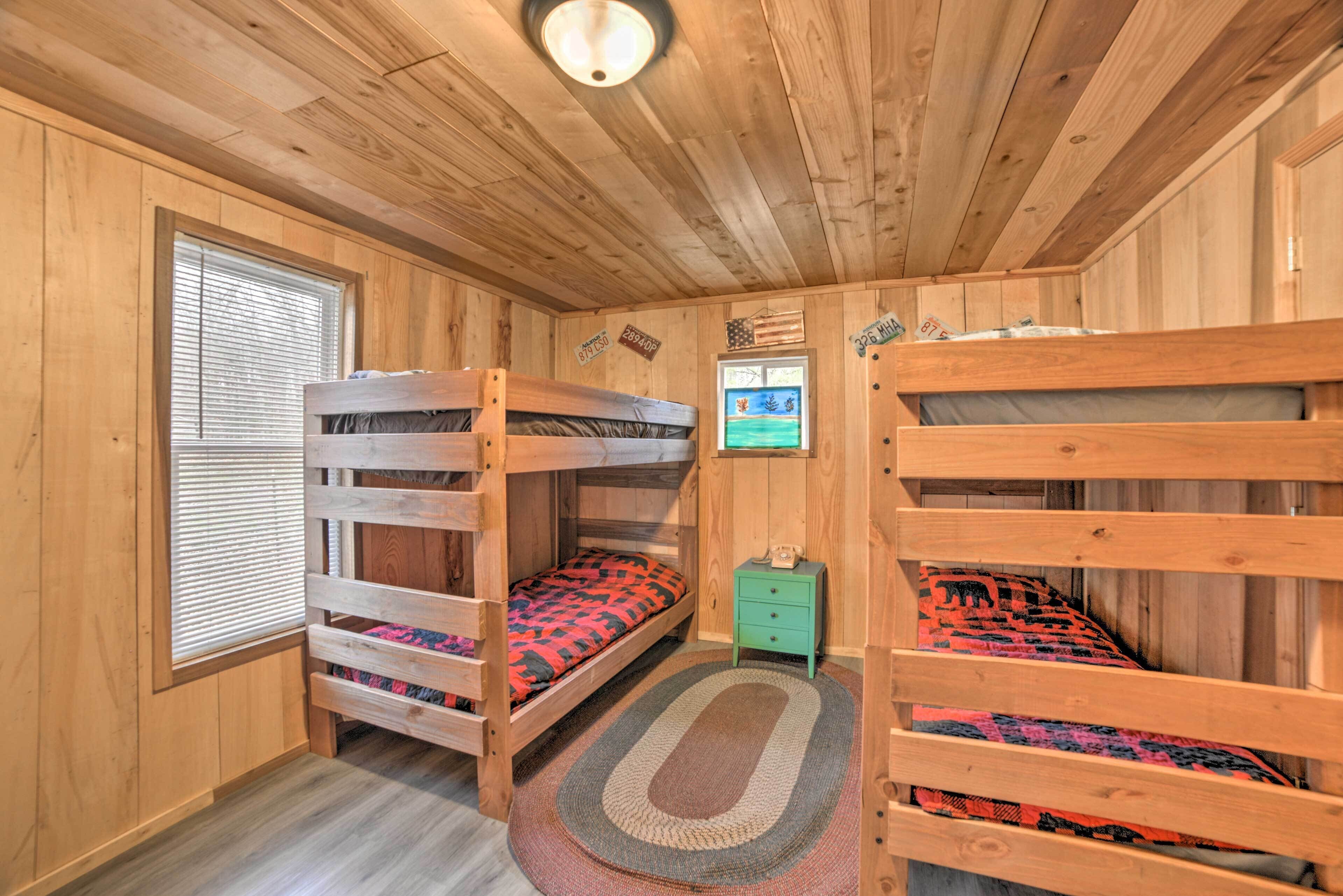 A wooden cabin room with bunk beds, a small desk, and a window with blinds.
