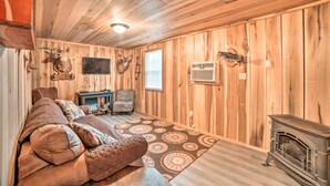 A cozy room with wooden walls, a sofa, a chair, a fireplace, and mounted animal heads. - Remote Kentucky Cabin w/ Fire Pit & 2 Ponds (New Concord)
