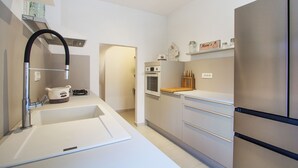 A modern kitchen with white cabinetry, a stainless steel refrigerator, a built-in oven, and a sink with a faucet.