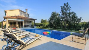 A pool area with lounge chairs, a floating pool toy, and a building with a tiled roof.