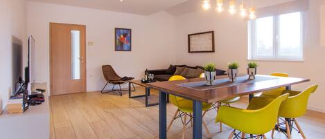 A modern living room with a sofa, a dining table with chairs, and a TV.