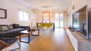 A modern living room with a sofa, a dining table with chairs, a TV, and a large window.