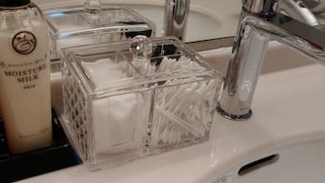 A bathroom sink with a bottle of Moisture Milk, a glass container with cotton swabs, and a Toto faucet.