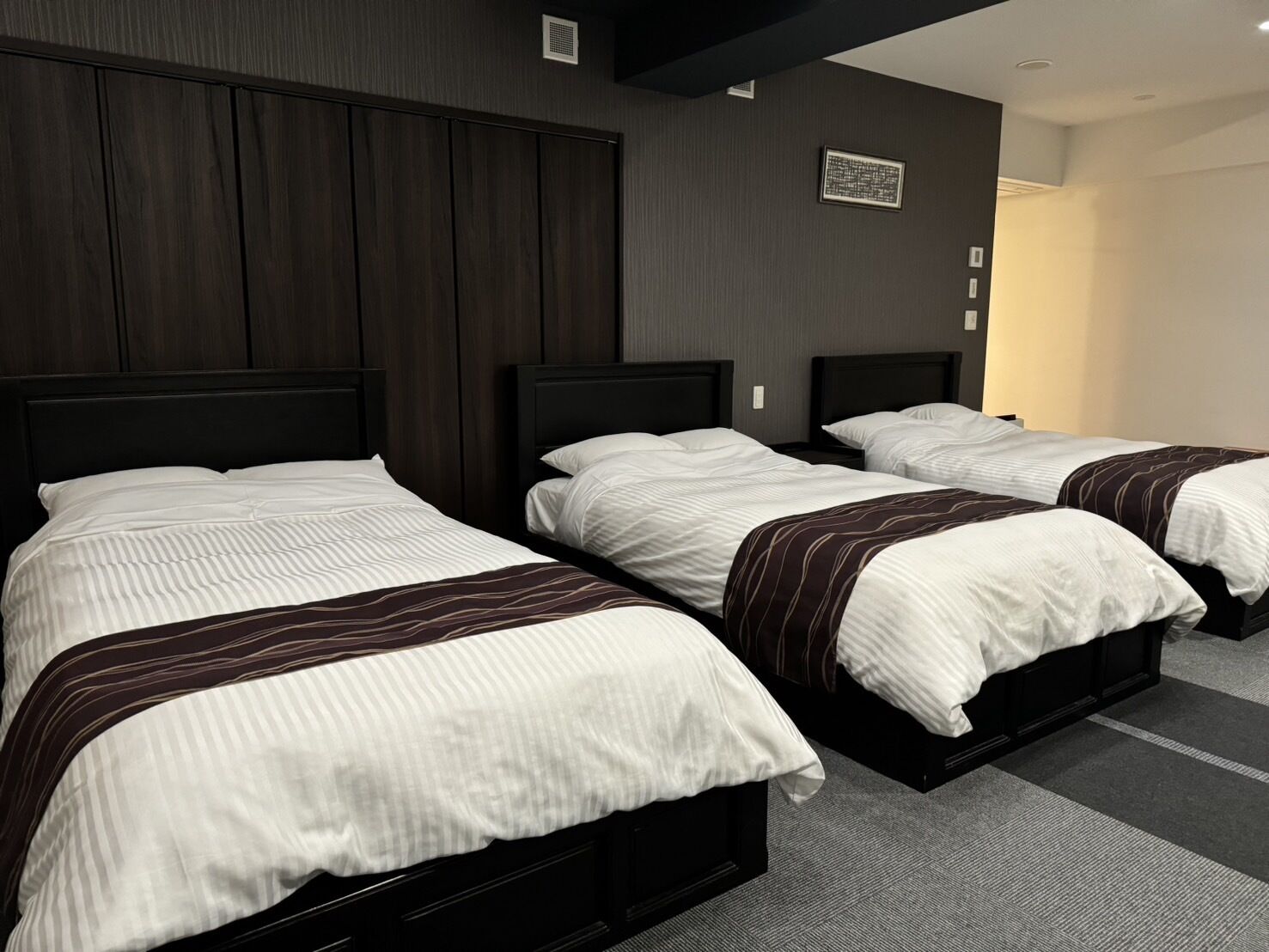 A hotel room with three beds, dark wood paneling on the walls, and a carpeted floor.