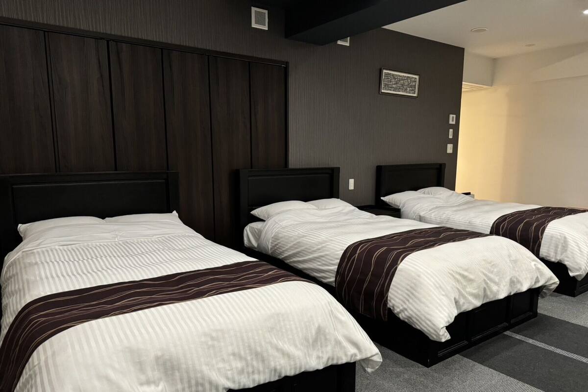 A hotel room with three beds, dark wood paneling on the walls, and a carpeted floor.