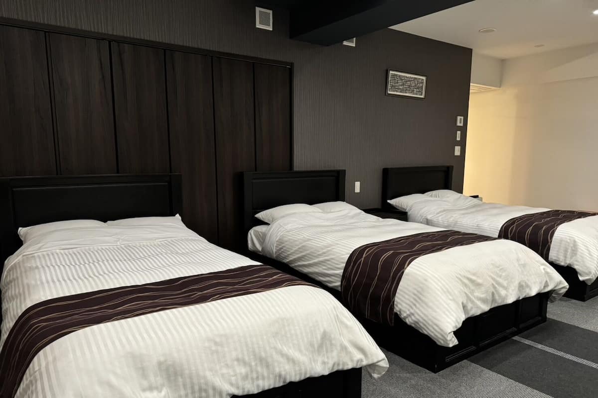 Habitación de hotel con tres camas, paneles de madera oscura en las paredes y suelo alfombrado.