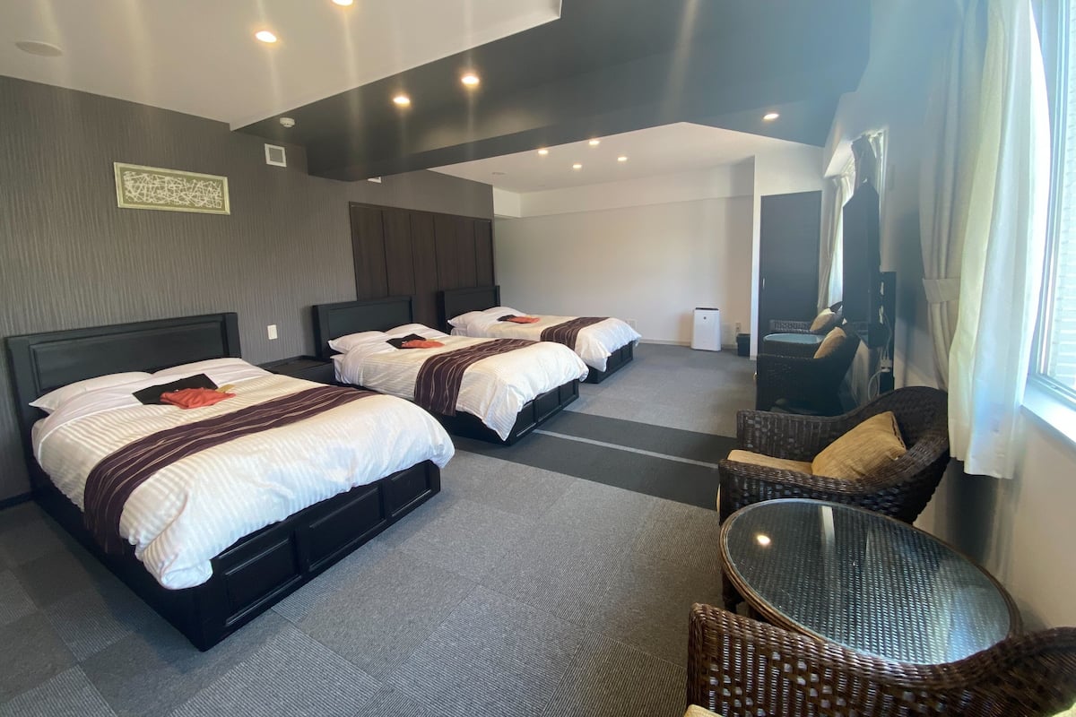 A hotel room with three beds, a small table, and a chair.