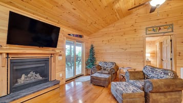 A log cabin interior with a fireplace, a television mounted on the wall, and a Christmas tree.