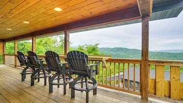 Een houten terras met vier Adirondack-stoelen en een houten tafel, met uitzicht op een bergachtig landschap.