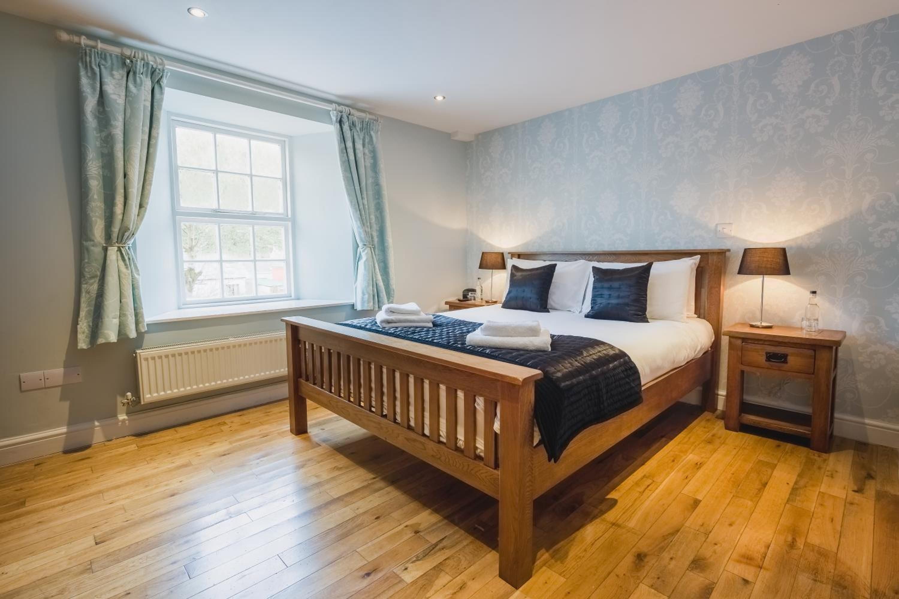 A bedroom with a wooden bed, two bedside tables, a window with curtains, and a radiator.