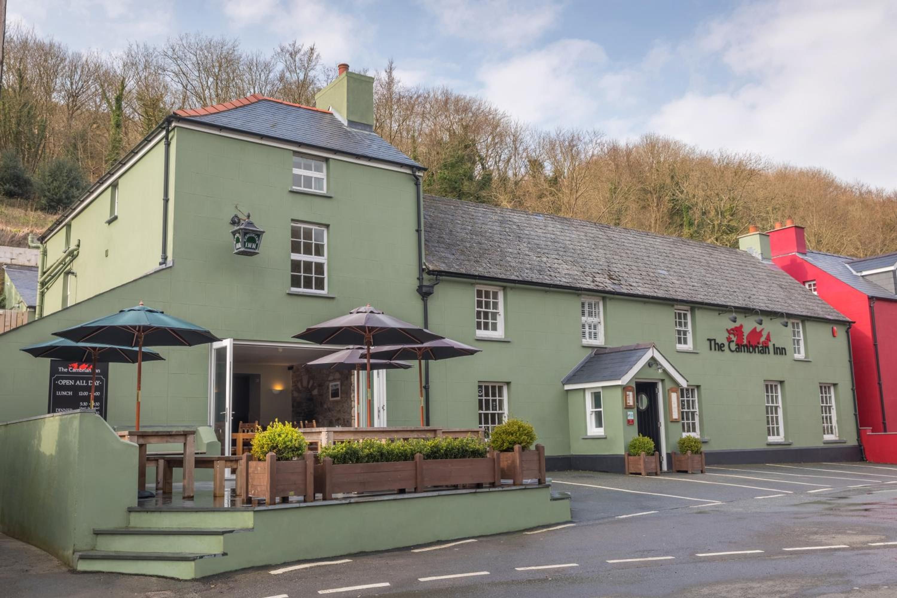 A green building with a sign for 'The Cambrian Inn' and outdoor seating with umbrellas.
