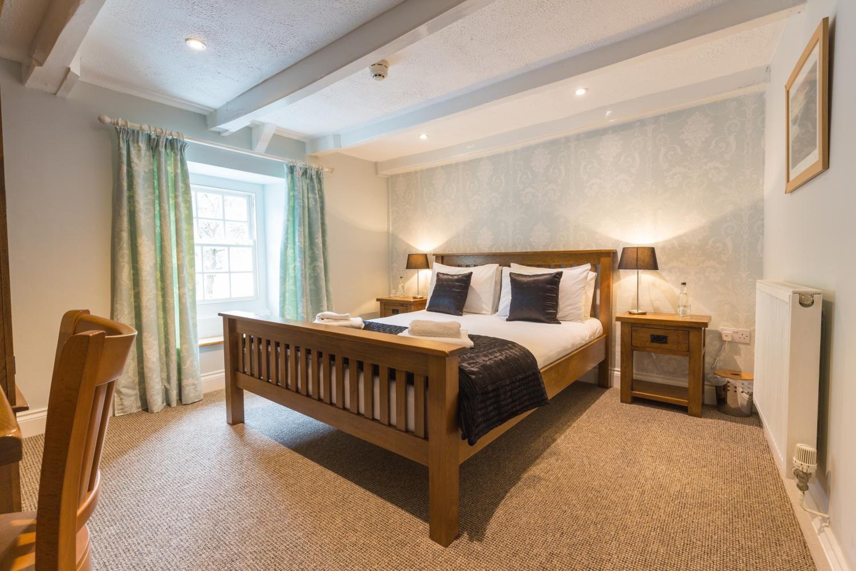 Une chambre à coucher avec un lit en bois, deux tables de chevet, une fenêtre avec des rideaux et un radiateur.