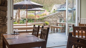 An outdoor dining area with wooden tables and chairs, stone walls, and umbrellas.