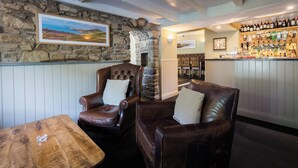 A cozy bar area with stone walls, leather chairs, a wooden table, and a well-stocked bar with various bottles and glasses.