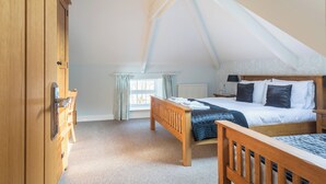 A bedroom with a sloped ceiling, a wooden bed, a nightstand, a dresser, and a window with curtains.