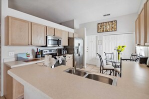 A modern kitchen with wooden cabinets, stainless steel appliances, a dining area with chairs, and a vase with flowers.