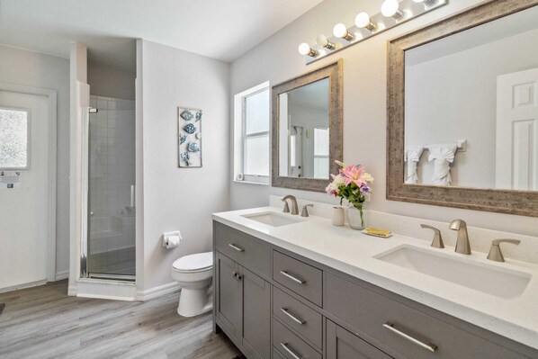 A modern bathroom with a shower, toilet, vanity with dual sinks, and a large mirror.