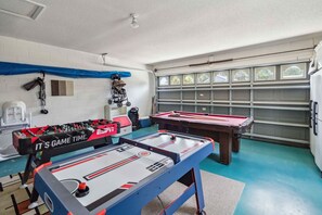 Een kamer met een tafelvoetbaltafel, een pooltafel en een garagedeur met ramen.