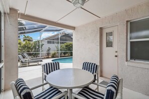 Een overdekt terras met een zwembad, buitenmeubels en een deur naar het huis.