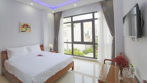 A hotel room with a bed, a TV, a window with curtains, a painting, and a vase with flowers. - Summer Beach (Da Nang)