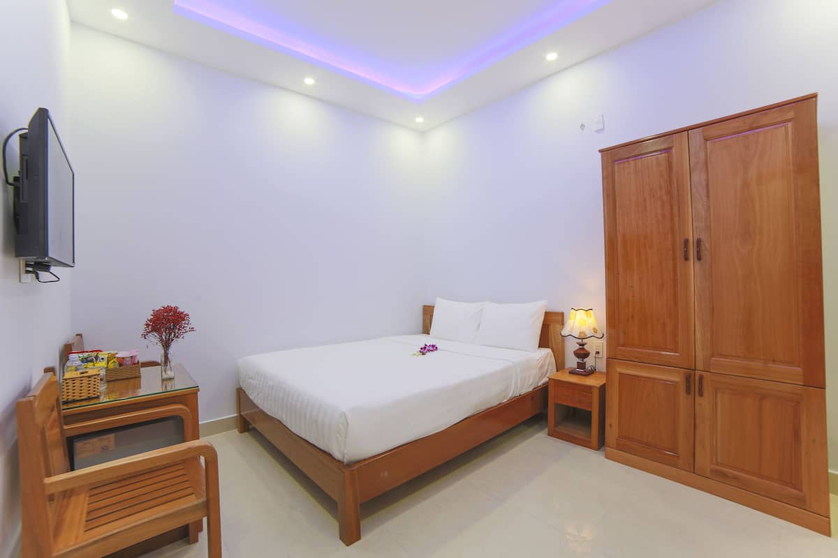 A bedroom with a bed, bedside table, lamp, wooden wardrobe, and a television on the wall.